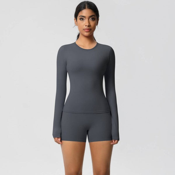 Woman in dark gray, long-sleeve top and shorts, standing against a light gray background.