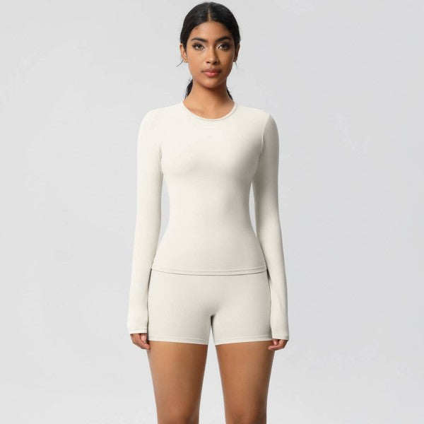 Woman in a fitted cream long-sleeve top and shorts against a light gray background.