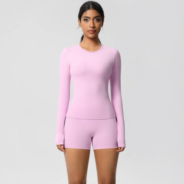 Woman in pink long-sleeve top and shorts, standing against a gray background.