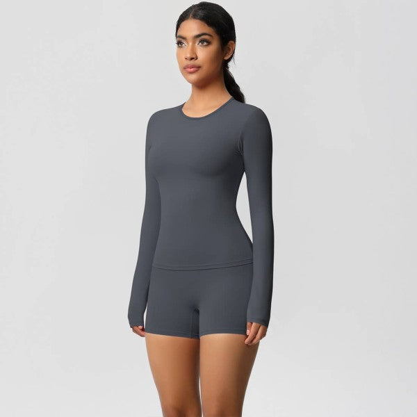 Woman in dark gray long-sleeve top and shorts on light gray background, standing confidently.