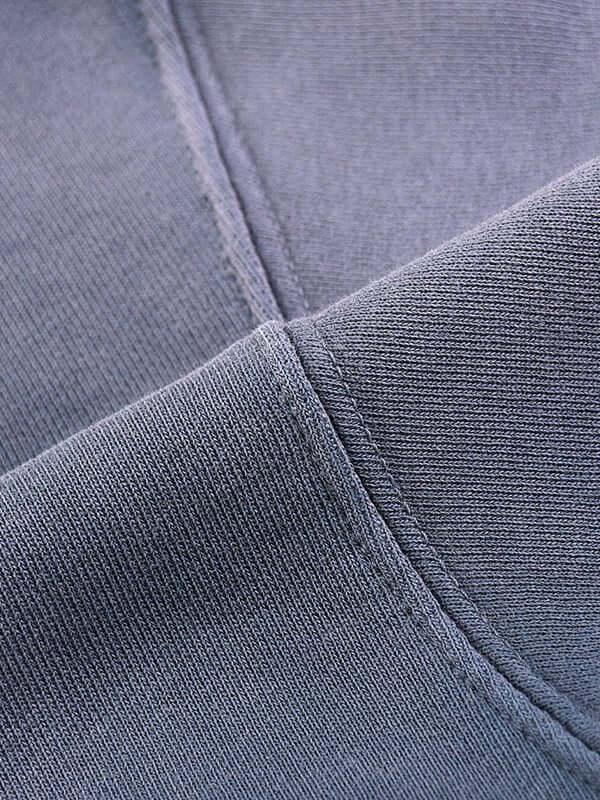 Close-up of intersecting seams on soft, gray fabric, showing texture and stitching details.