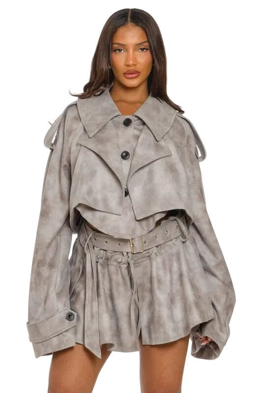 Woman in oversized gray jacket and shorts, with black buttons and a wide belt, on a light background.