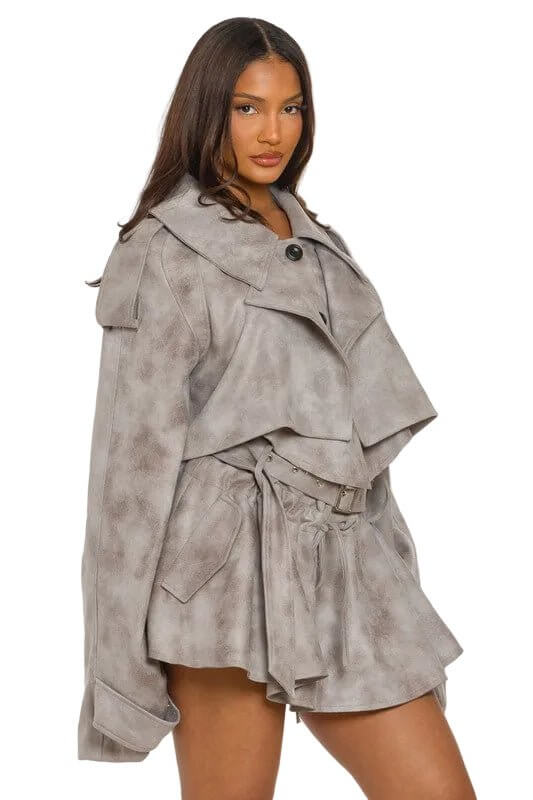 Woman in a light gray oversized jacket and skirt with a tie belt, against a white background.