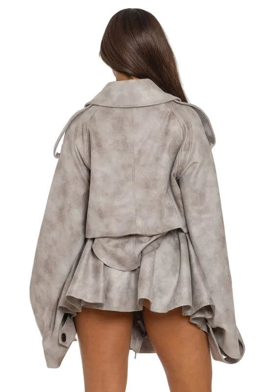 Woman in oversized, textured gray jacket with a short skirt, facing away against a light background.