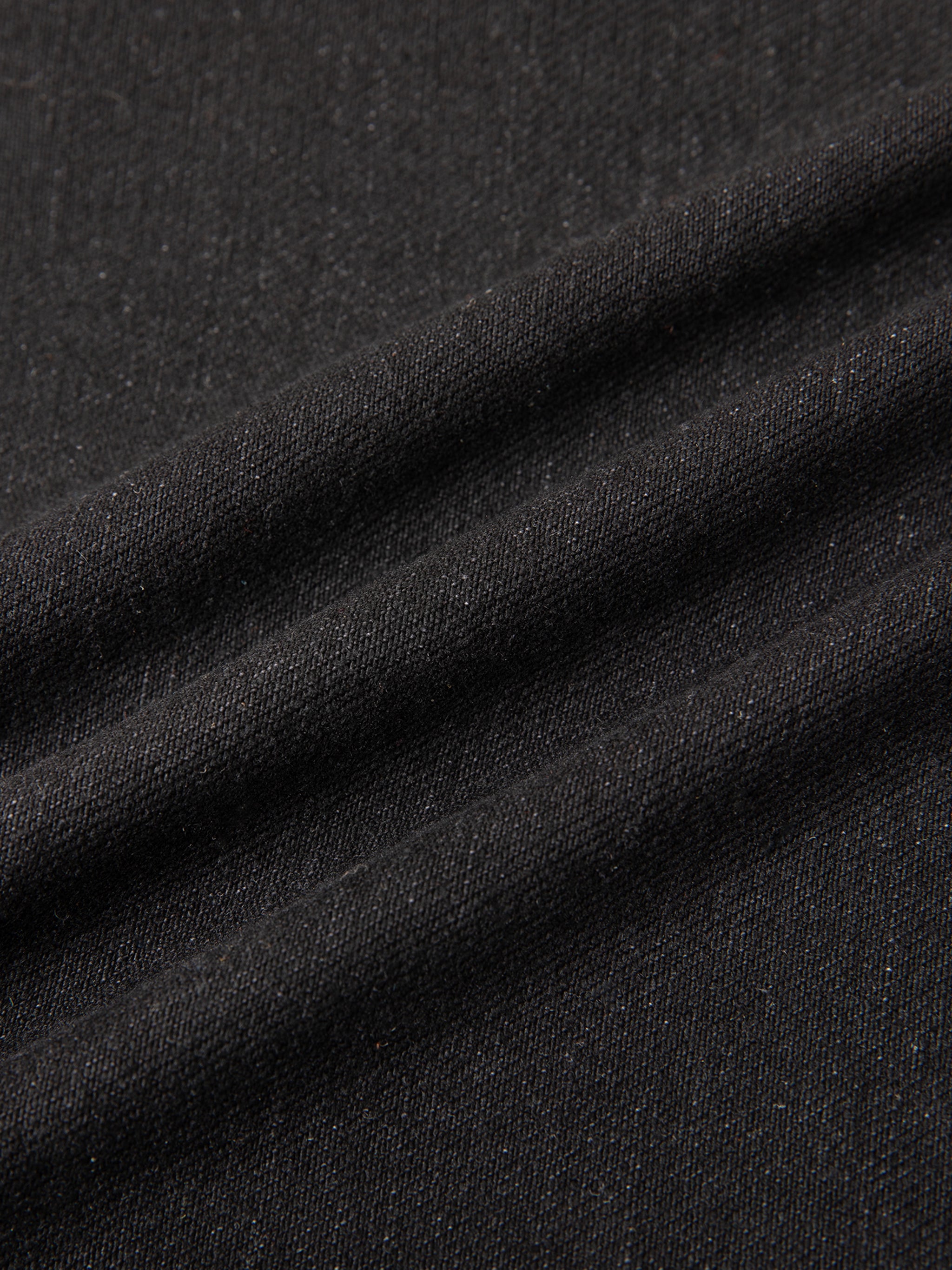 Close-up of black textured fabric with diagonal folds and subtle sheen.