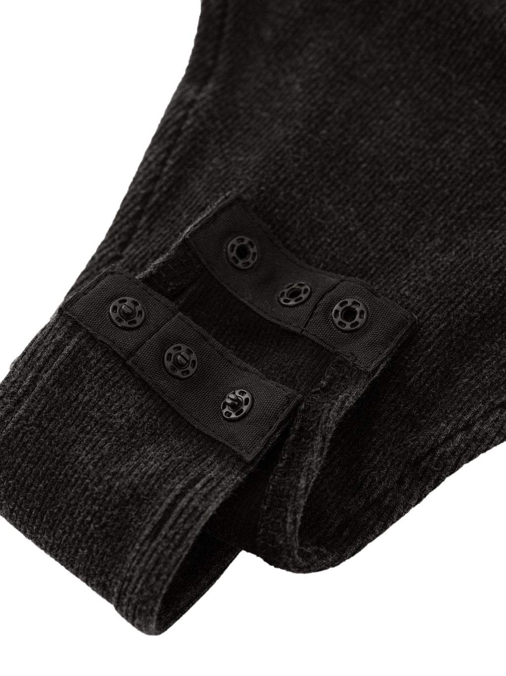 Close-up of a black knitted fabric with snap buttons on a flap, showing texture and detail.